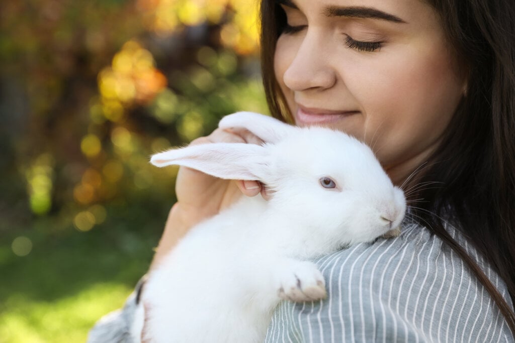 Happy woman with cute rabbit outdoors on sunny day, closeup.